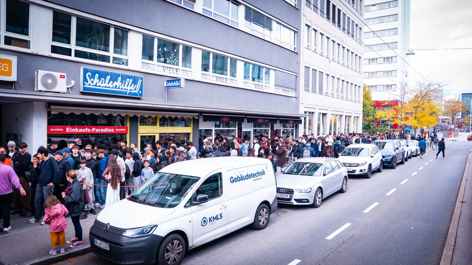 Lange Warteschlange entlang der Häuserfront vor dem Lokal, daneben parkende Autos auf der Straße