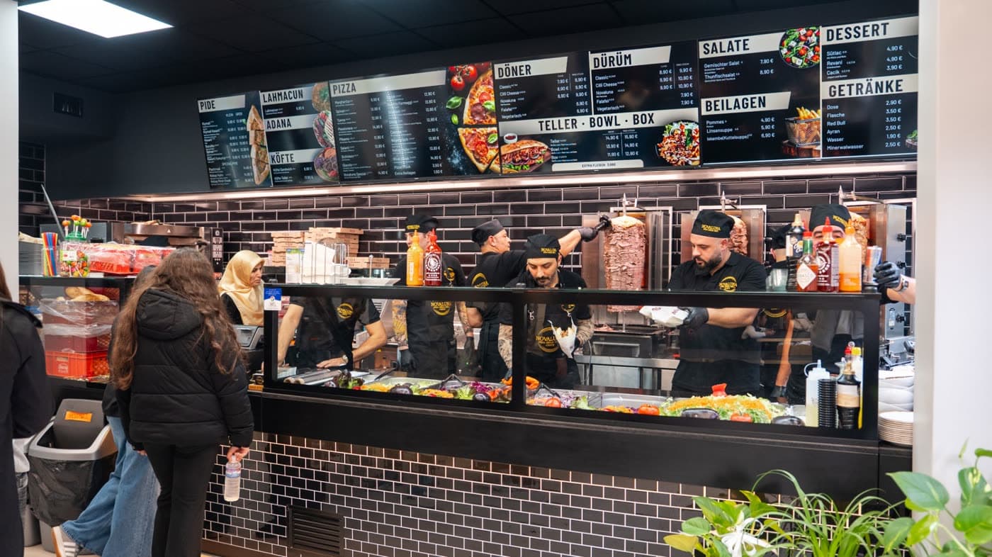 Blick in das Lokal mit Menütafeln und dem Team hinter der Theke